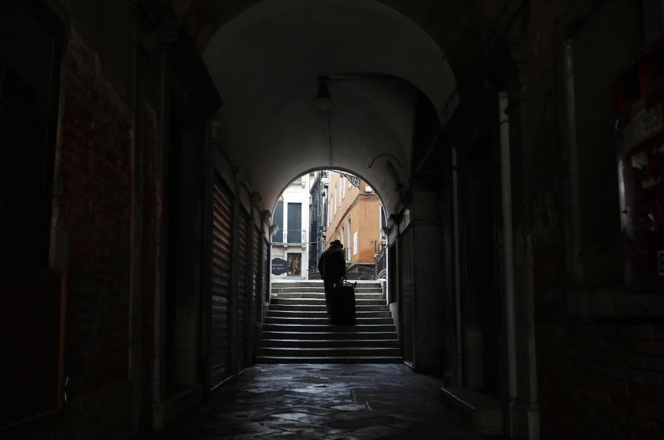 A man walks in an empty St. Mark's square arcade in Venice, Italy, Saturday, Jan. 30, 2021. Gondolas and other vessels are moored instead of preparing for Carnival's popular boat parade in the lagoon. Alleys are eerily empty. Venetians and the city's few visitors stroll must be masked in public places, indoors and out, under a nationwide mandate. (AP Photo/Antonio Calanni)