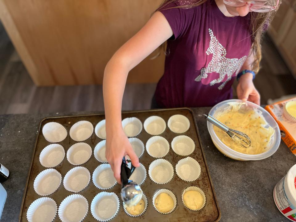 lisa's daughter spooning cupcake batter into a lined cupcake tin