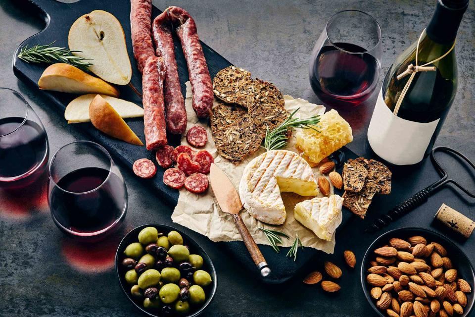 <p>Tracey Kusiewicz / Foodie Photography / Getty Images</p> Wine and a charcuterie and cheese platter, with pears nuts and olives