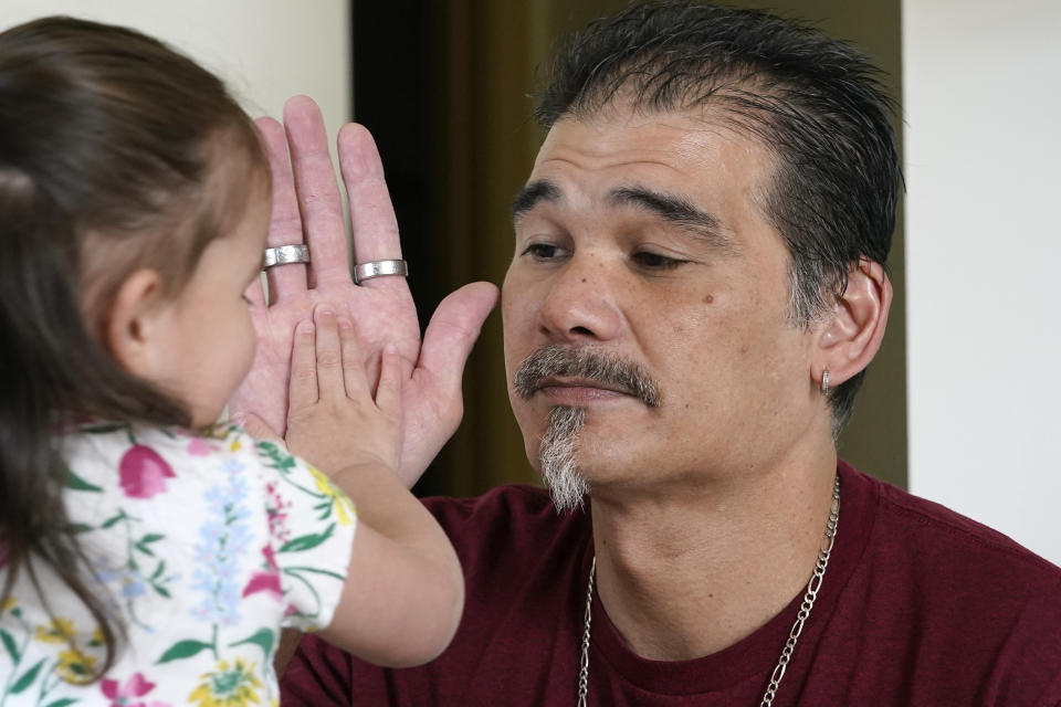Leroy Pascubillo touches hands with his daughter, who was born addicted to heroin and placed with a foster family at birth, May 10, 2021, in Seattle. Pascubillo, who had used drugs for the better part of four decades, was in a court-ordered in-patient drug rehab program when the pandemic first hit. (AP Photo/Elaine Thompson)