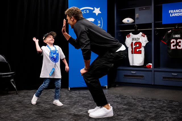 <p>Fanatics</p> Tom Brady gives high five to child in locker room at Fanatics and Make-A-Wish event