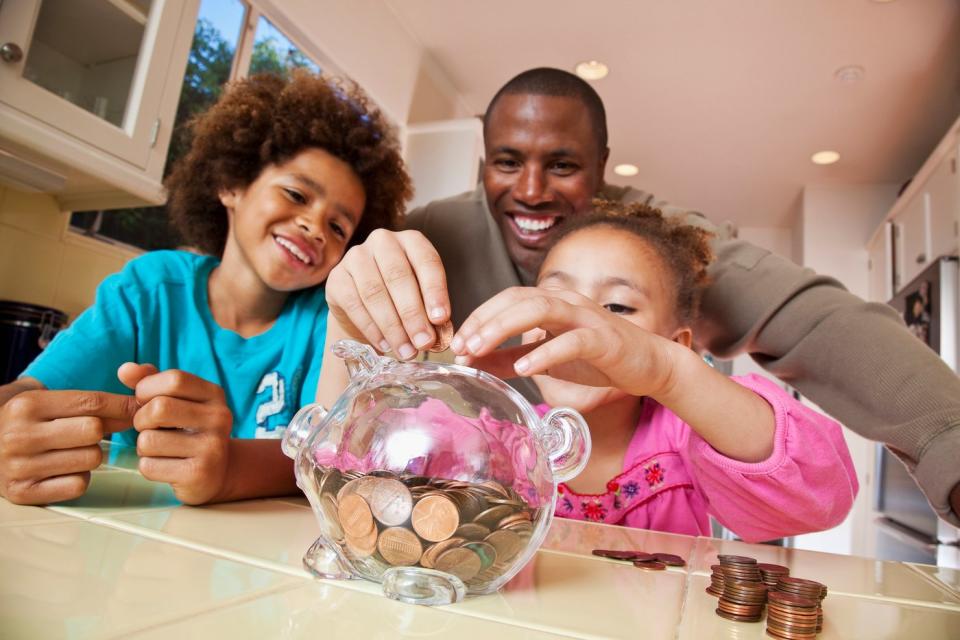 A father puts coins in a piggy bank with his two children.