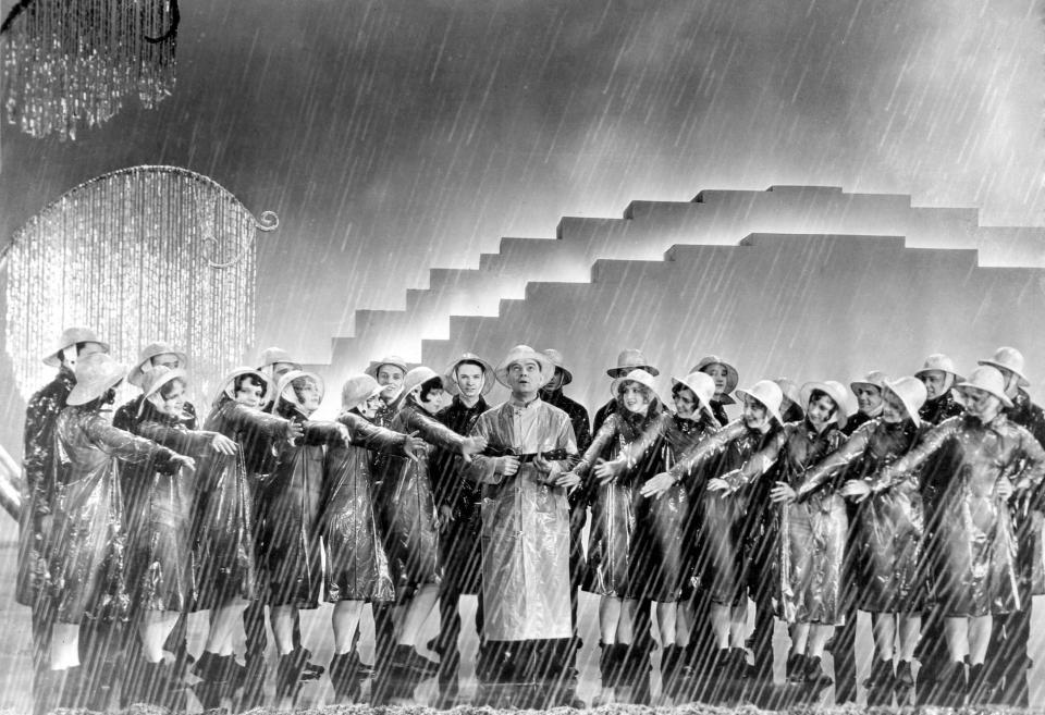 A scene from the film "Singing in the rain" with Gene Kelly, Debbie Reynolds and a group of dancers in raincoats and hats performing in the rain