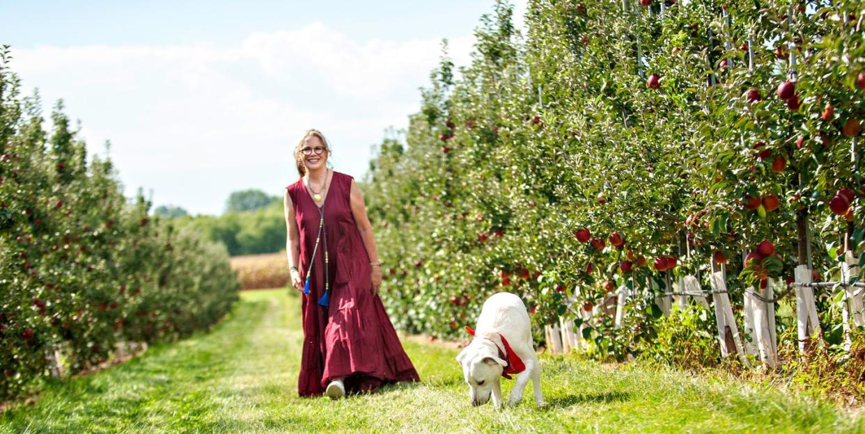 melissa gilbert in red long dress walking in apple orchard with dog