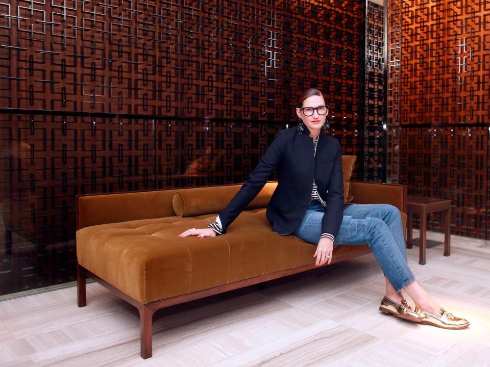 J. Crew's Jenna Lyons sits on brown velvet couch wearing blazer, jeans, and loafers