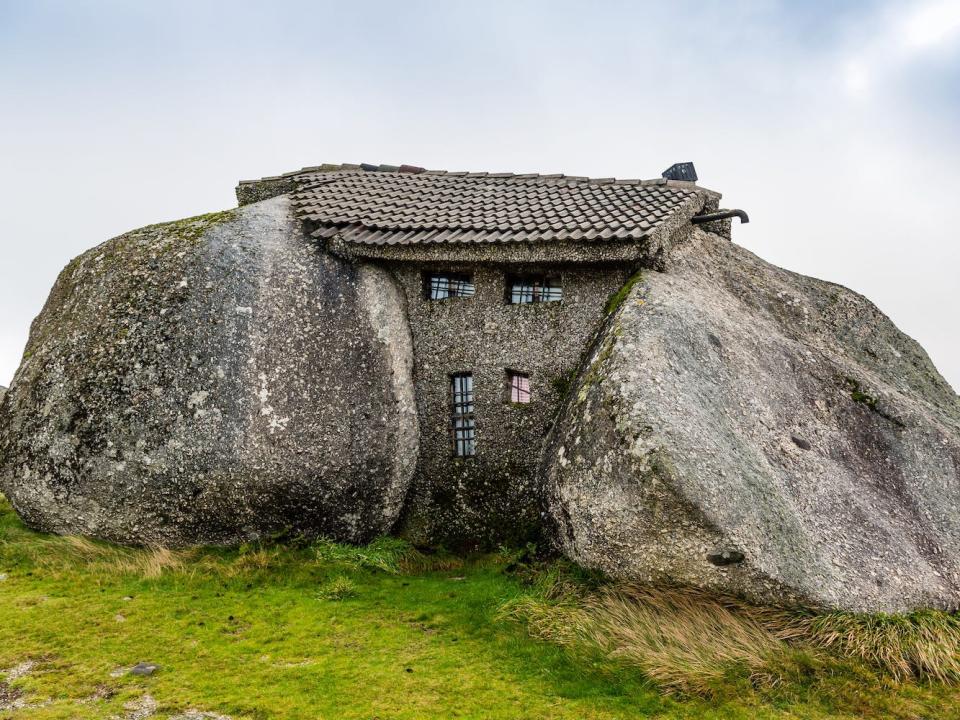 A house is visible between two large rocks.