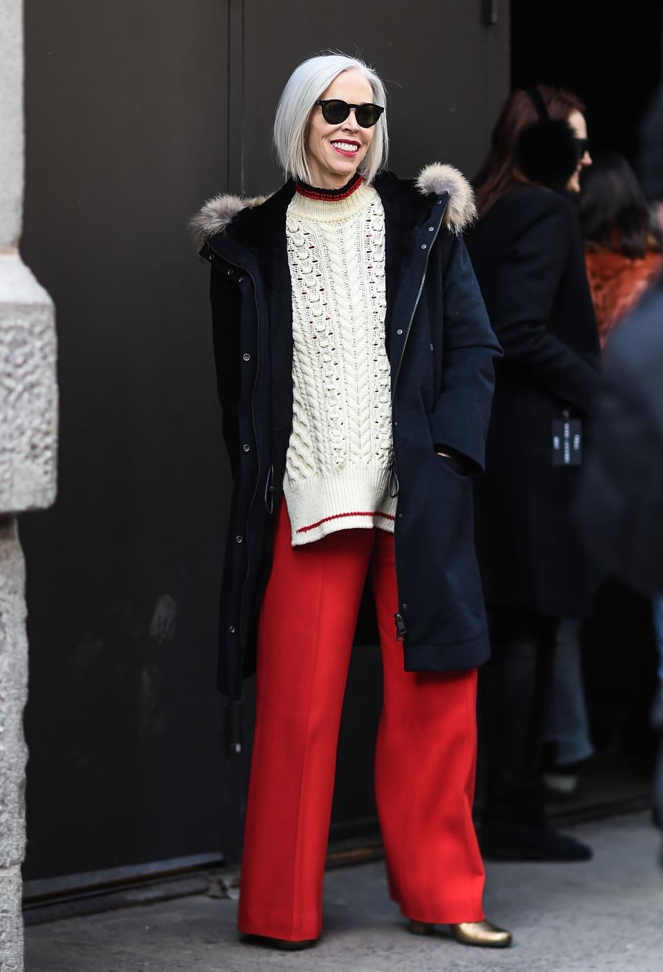 <p>Linda Fargo, fashion director at Bergdorf Goodman, wears a parka, cableknit sweater, bright red, wide-legged trousers, gold booties, and a chic pair of wayfarers. Whether you’re 25 or 55, this is a great look for all. (Photo: Getty) </p>