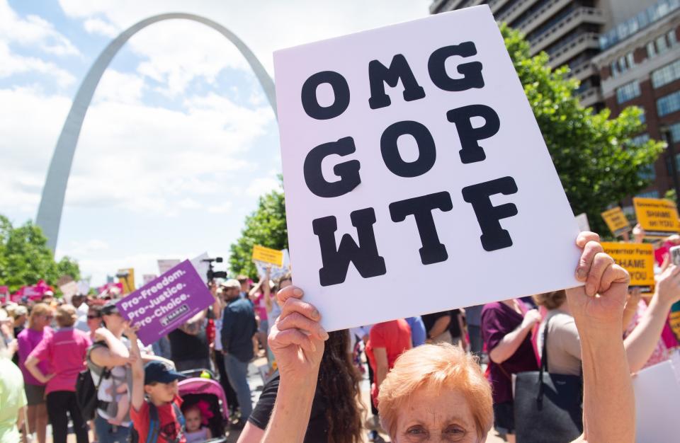 A protester standing near the Gateway Arch in St. Louis holds a sign reading "OMG GOP WTF"