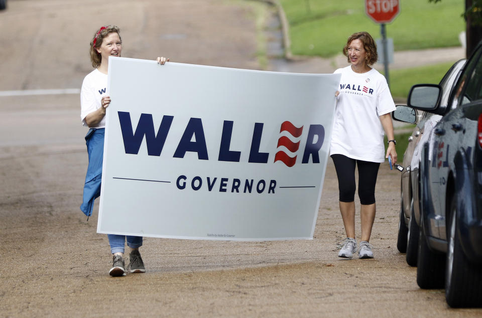 Sisters-in-law Bae Waller, left, and Yonnie Waller, of former Mississippi Supreme Court Chief Justice Bill Waller Jr., a candidate for the GOP nomination for governor, rush to get his campaign sign out of the rain at a north Jackson, Miss., precinct, Tuesday, Aug. 27, 2019. Waller faces Lt. Governor Tate Reeves in the runoff for the Republican Party nomination for governor. (AP Photo/Rogelio V. Solis)