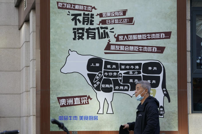 A man carries his meal past an advertisement promoting imported beef from Australia in Beijing, Monday, Nov. 23, 2020. China has stirred controversy with claims it has detected the coronavirus on packages of imported frozen food. (AP Photo/Ng Han Guan)