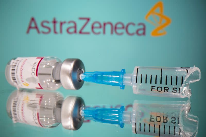 Vial labelled with broken sticker "AstraZeneca COVID-19 Coronavirus Vaccine" and a broken syringe are seen in front of a displayed AstraZeneca logo in this illustration