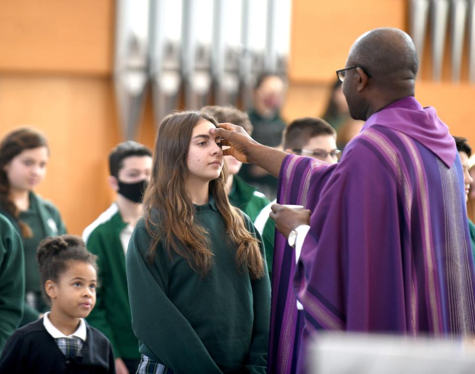 Rev. Benson Okpara applies ashes to the forehead of St. Michael's School eighth grader Olivia Johnston during Ash Wednesday Mass.