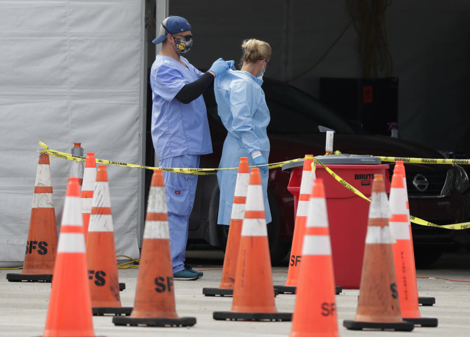 FILE - In this July 5, 2020, file photo, healthcare workers help each other with their personal protective equipment at a drive-thru coronavirus testing site outside Hard Rock Stadium in Miami Gardens, Fla. The PPE that was in dangerously short supply during the initial weeks of the coronavirus crisis in the U.S. is running out again as the virus resumes its rapid spread and the number of hospitalized patients climbs. (AP Photo/Wilfredo Lee, File)