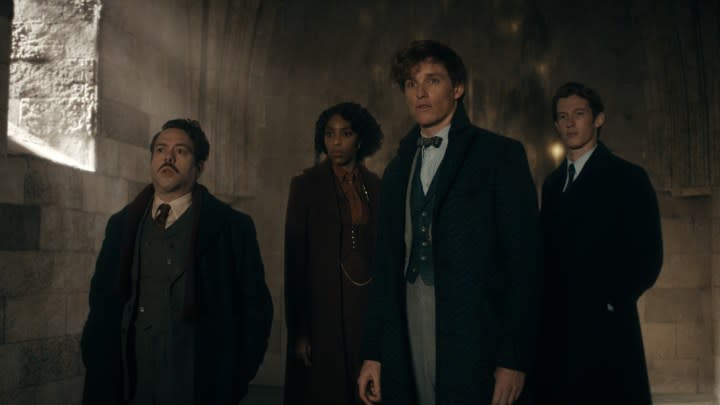 Eddie Redmayne, Dan Fogler, and the cast of Fantastic Beasts: The Secrets of Dumbledore walk down a dark hallway.