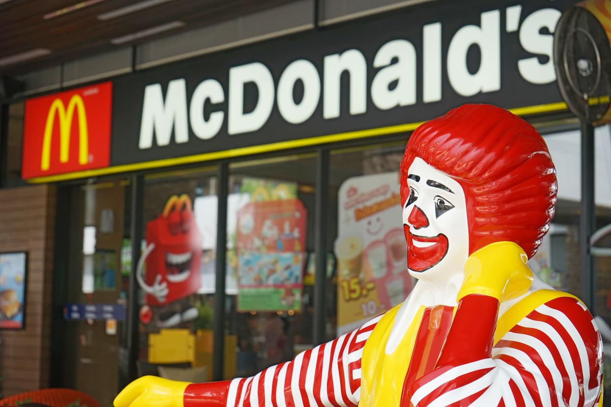 Ronald McDonald sitting statue cropped in the right foreground with blurred McDonald's restaurant in the background, Bangkok, Thailand