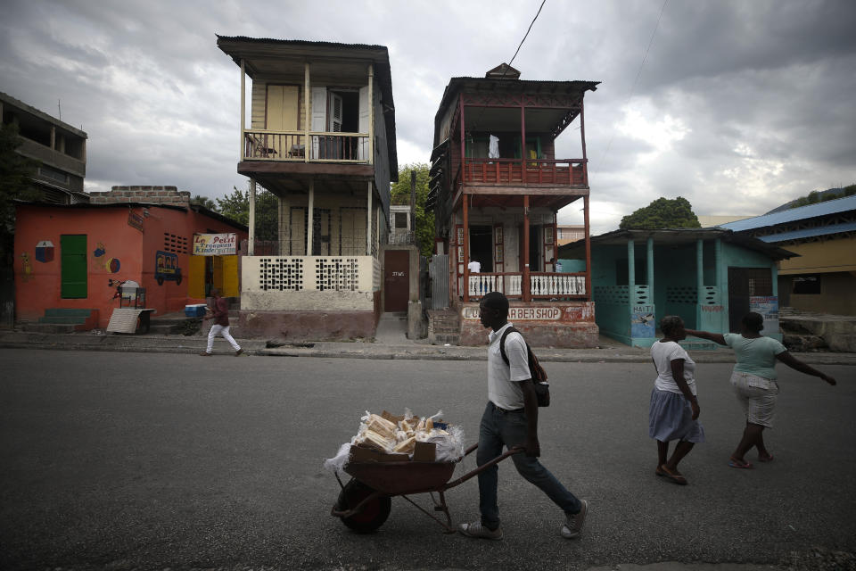 A bread vendor wheels his stock past a pair of old wooden homes in central Port-au-Prince, Haiti, Wednesday, Oct. 2, 2019. Violent protests have shuttered public schools and businesses and left Haiti's economy sputtering amid ballooning inflation, as opposition leaders and their supporters demand the resignation of President Jovenel Moise. (AP Photo/Rebecca Blackwell)