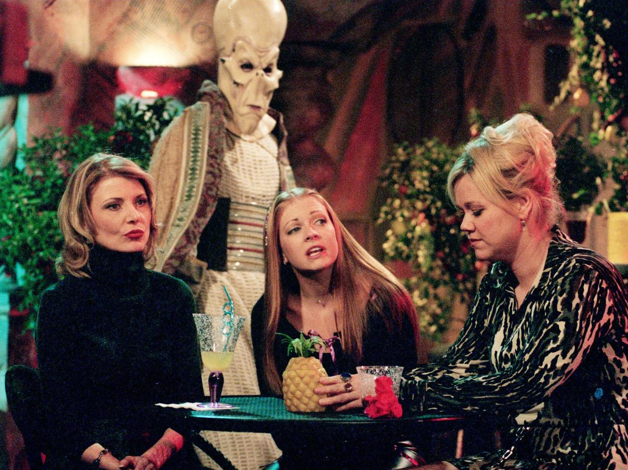 Melissa Joan Hart, star of the WB network series "Sabrina, the Teenage Witch," sits with series co-stars Beth Broderick, left, and Caroline Rhea, who play fellow witches Zelda and Hilda, respectively, as an alien figure passes behind them during a break from shooting on the series set at Paramount Studios Oct. 6, 2000, in Los Angeles. (AP Photo/Reed Saxon)