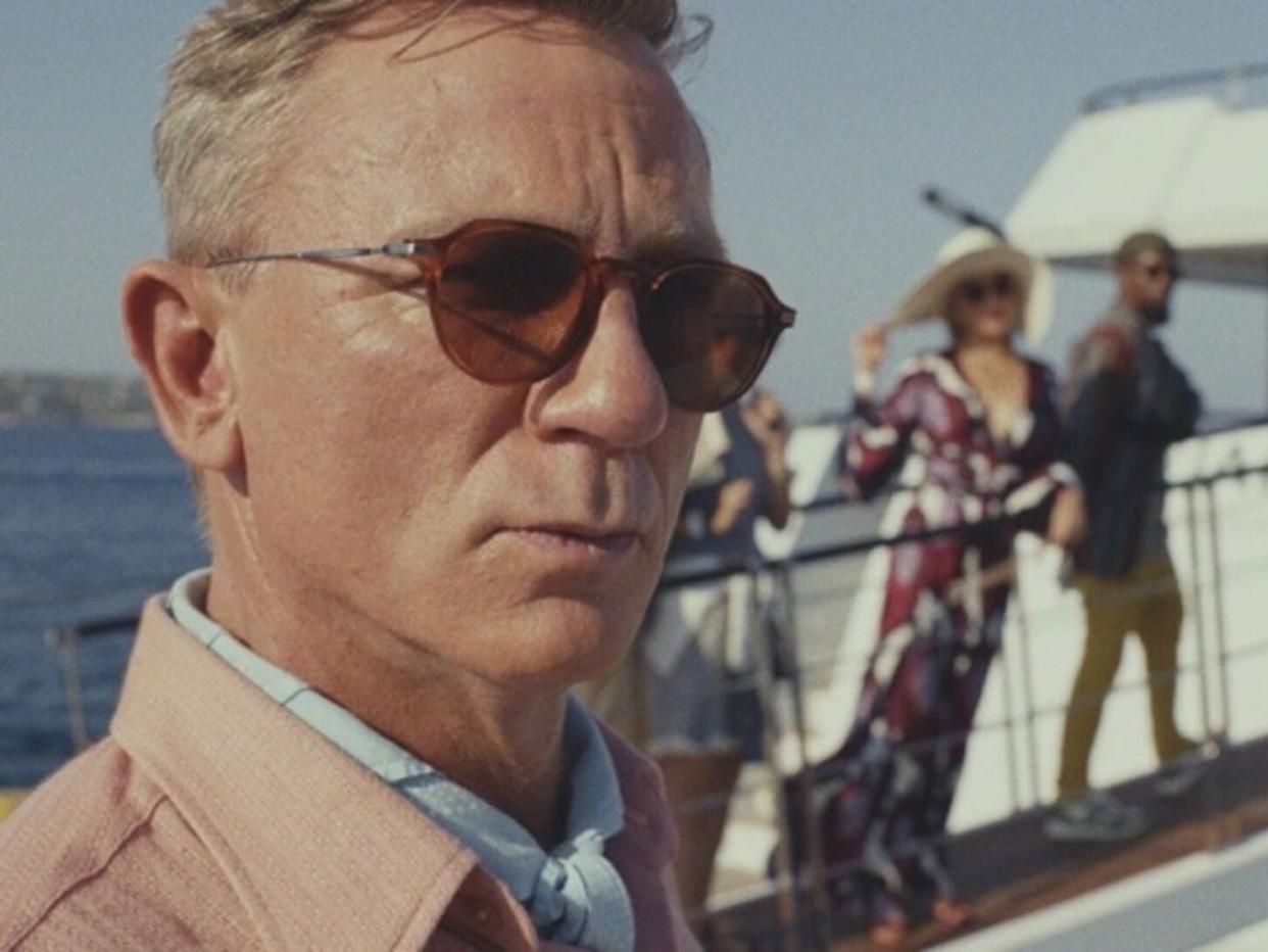 Daniel Craig in sunglasses, people behind him on a bridge to a boat