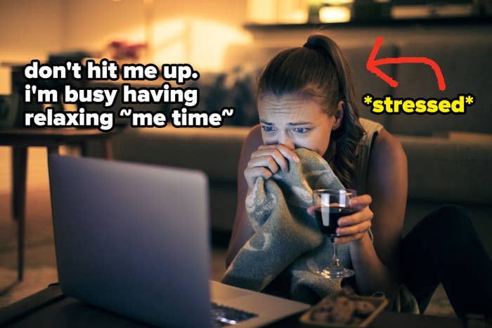 woman holding glass of wine and blanket while stressfully watching laptop screen