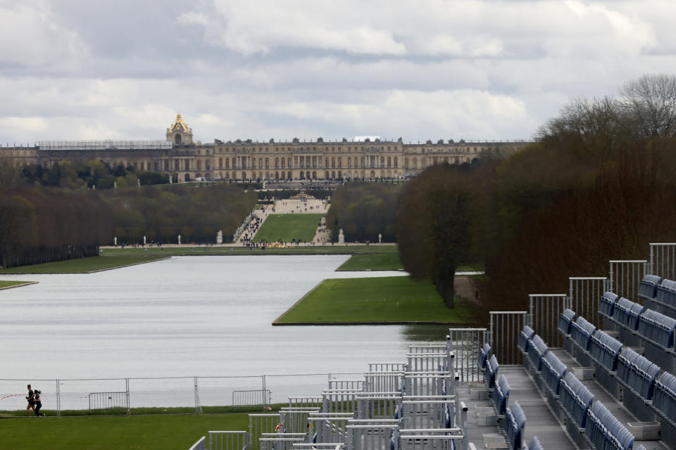 FILE - A couple jogs past the stands to watch the equestrian sports, Friday, March 29, 2024 in the park of the Chateau de Versailles, west of Paris. The site will be the venue for equestrian sports at the Paris 2024 Olympic Games. The Chateau de Versailles is seen in background. Once the residents of French royalty. Louis XVI _ the Sun King _ and Marie Antoinette held lavish banquets before the French revolution led to their executions. During the Paris Games, equestrian riders will gallop at the heart of the palace's gardens and odern pentathlon events also take place there. (AP Photo/Thomas Padilla, File)