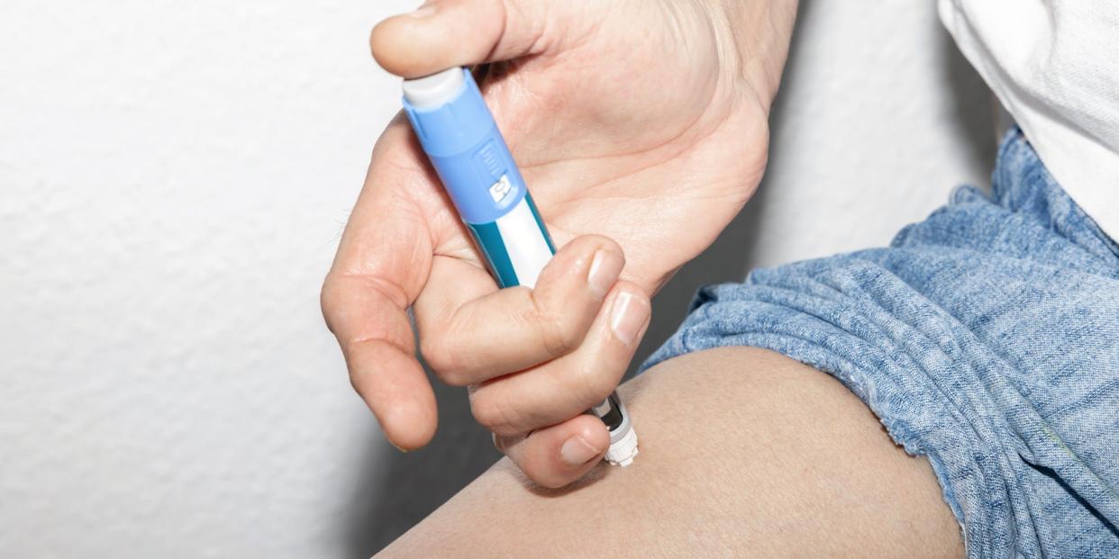 a close up of a person using an injector pen for medication to treat diabetes, applying the pen to their leg