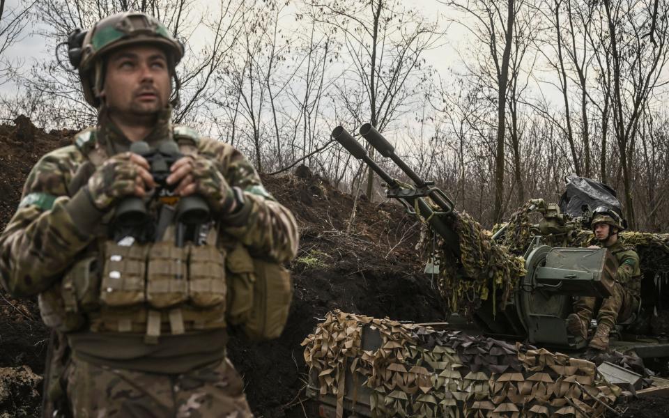 A Ukrainian serviceman (L) looks on and holds binoculars next to another (R) sitting on an anti-air gun near Bakhmut, on March 24, 2023. (Photo by Aris Messinis / AFP) (Photo by ) - ARIS MESSINIS/AFP via Getty Images