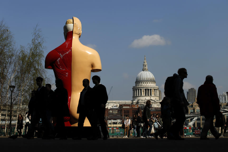 People are silhouetted in the shade as they walk past the back of British artist Damien Hirst's 1999-2005 piece "Hymn", a painted bronze, as St Paul's Cathedral can be seen on the other side of the River Thames in the background during a media preview of the first substantial show of his work in the UK at the Tate Modern gallery in London, Monday, April 2, 2012.  The exhibition, timed for the culmination of the Cultural Olympiad and due to open to the public on Wednesday, showcases over 70 of Hirst's works since he first came to public attention in 1988.  (AP Photo/Matt Dunham)