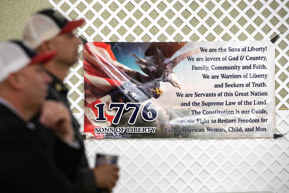 People stand near a banner that reads "We are the sons of liberty. We are lovers of God & Country."