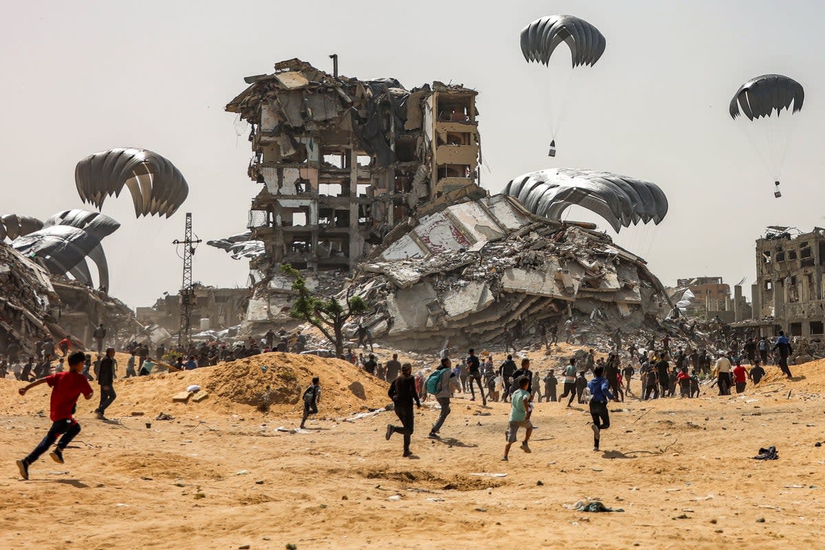 People rush to landing humanitarian aid packages dropped over the northern Gaza Strip on 23 April, 2024 (AFP via Getty)