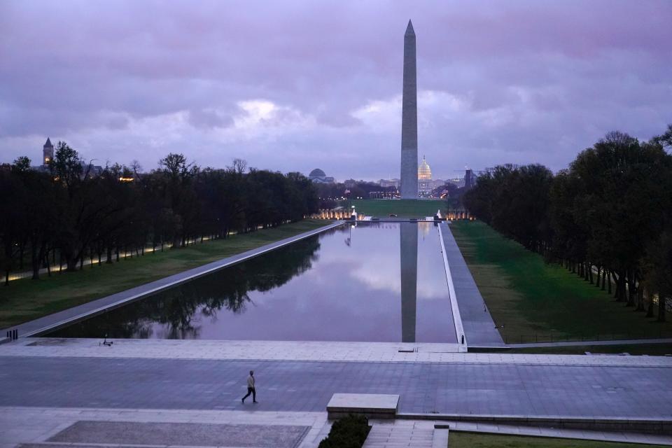 A man walks past the Lincoln Memorial Reflecting Pool and Washington Monument as sunrise approaches on Thanksgiving, Thursday, Nov. 26, 2020, in Washington.