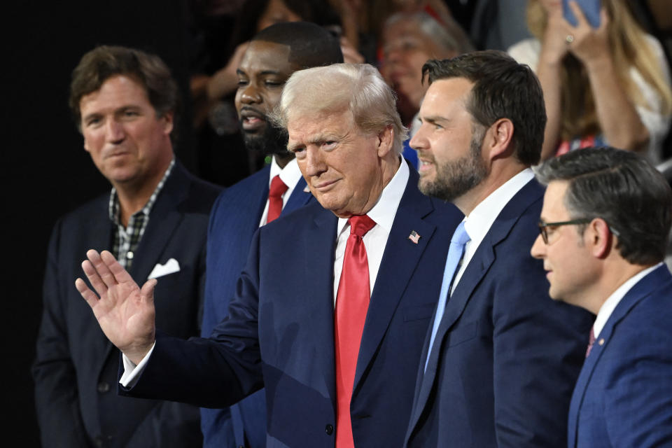 Former US President and 2024 Republican presidential candidate Donald Trump waves as he arrives to his seat during the first day of the 2024 Republican National Convention at the Fiserv Forum in Milwaukee, Wisconsin, July 15, 2024. Also picutred (L-R) US political commentator Tucker Carlson, US Representative of Florida Byron Donalds, US Senator from Ohio and Republican vice presidential candidate J. D. Vance  and US Speaker of the House Mike Johnson. Donald Trump won formal nomination as the Republican presidential candidate and picked a right-wing loyalist for running mate, kicking off a triumphalist party convention in the wake of last weekend's failed assassination attempt. (Photo by ANDREW CABALLERO-REYNOLDS / AFP) (Photo by ANDREW CABALLERO-REYNOLDS/AFP via Getty Images)