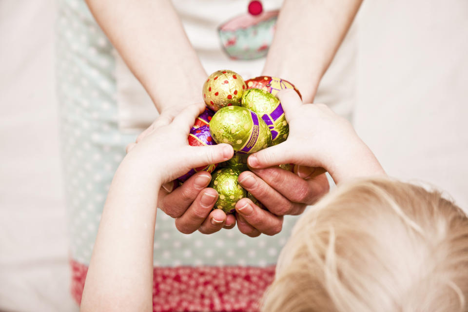 Mum offering a selection of brightly colored chocolate Easter eggs to a child.