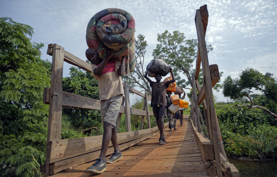 FILE - In this Thursday, June 8, 2017 file photo, from left, South Sudanese refugees Thomas Wani, 12, brother Peter Lemi, 14, mother Rose Sunday, and father Julius Lezu, cross a wooden bridge from South Sudan to Uganda at the Busia crossing, near Kuluba, in northern Uganda. The representative of the United Nations refugee agency in Uganda says "major gaps" in funding are constraining their work in the East African country sheltering 1.3 million refugees. Joel Boutroue told reporters in the Ugandan capital, Kampala, on Thursday, Sept. 12, 2019 that UNHCR in Uganda is operating at only 35% of the total requirements.(AP Photo/Ben Curtis, File)