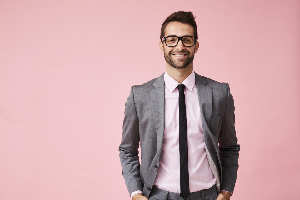 Smiling man in suit against pink background.