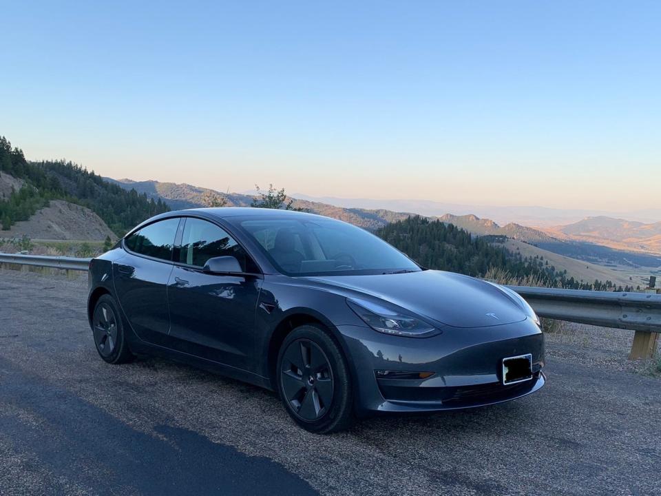 A dark gray Tesla Model 3 parked on a highway in Montana.