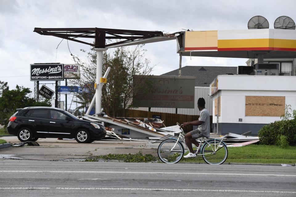 A person on a bicycle passes a damaged gas station.