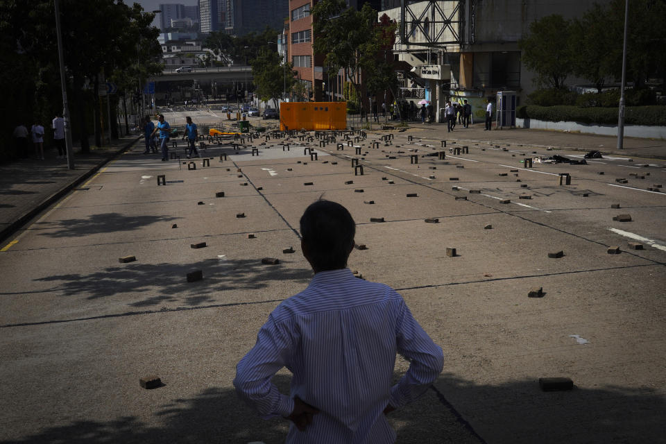 A man watches people cross a road littered with bricks and barricades set by pro-democracy protesters outside the Hong Kong Baptist University, in Hong Kong, Wednesday, Nov. 13, 2019. Police have increased security around Hong Kong and its university campuses as they brace for more violence after sharp clashes overnight with anti-government protesters. (AP Photo/Vincent Yu)