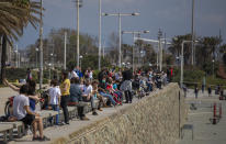 Families with their children sit in a boulevard as police patrol the beach, where access is prohibited, in Barcelona, Spain, Sunday, April 26, 2020 as the lockdown to combat the spread of coronavirus continues. On Sunday, children under 14 years old will be allowed to take walks with a parent for up to one hour and within one kilometer from home, ending six weeks of compete seclusion. (AP Photo/Emilio Morenatti)