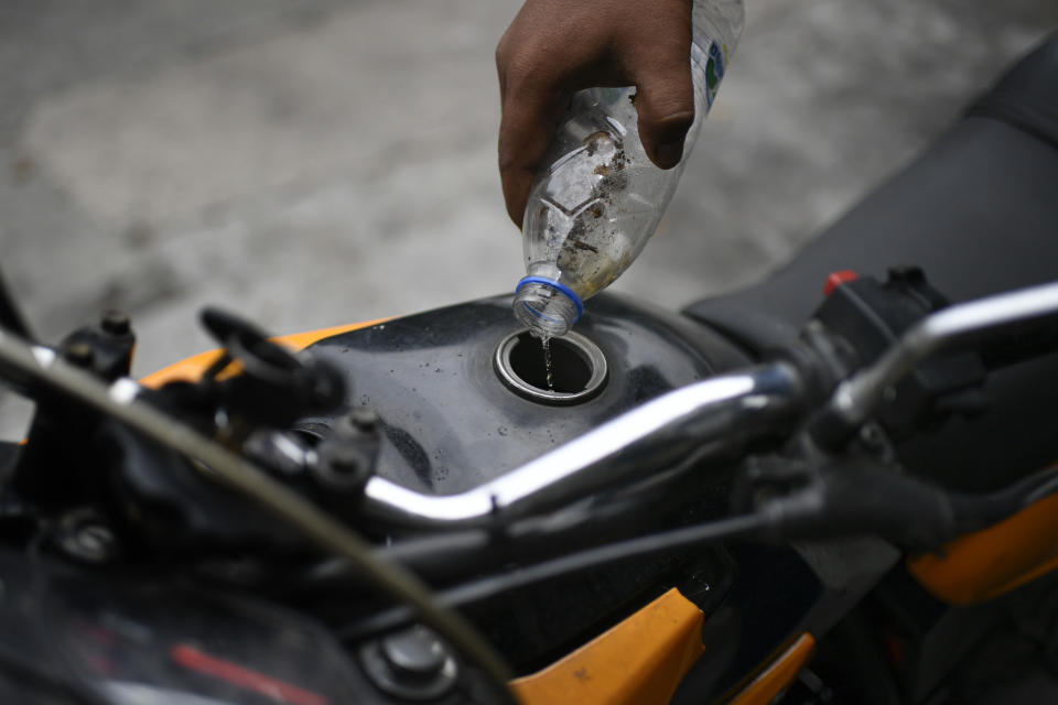 A biker drips in a few ounces of gasoline that he said he was able to catch from drops that dribbled from the pipe of a tanker as it supplied a gas station in Caracas, Venezuela, Sunday, May 31, 2020. After decades of being the cheapest gasoline in the world, Venezuelan President Nicolas Maduro indicates that as of next Monday a new pricing scheme will be imposed on some 200 stations. (AP Photo/Matias Delacroix)