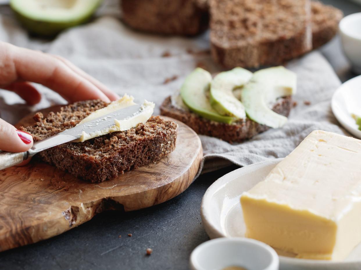 The girl spreads butter on whole wheat rye bread.