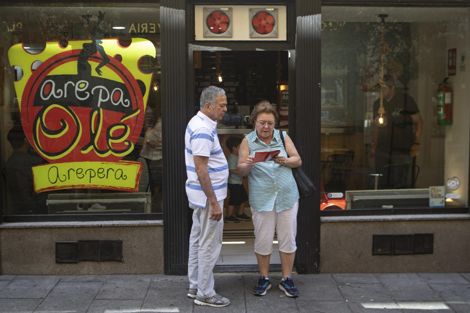 In this June 19, 2019 photo, a couple looks at a menu outside the Arepa Ole restaurant in Madrid, Spain, Wednesday, June 19, 2019. The arepa's surge on the world stage comes as consumption of the bread steadily declines back home amid a punishing financial crisis worse than the U.S. Great Depression, leading an estimated 4 million people to flee. (AP Photo/Paul White)
