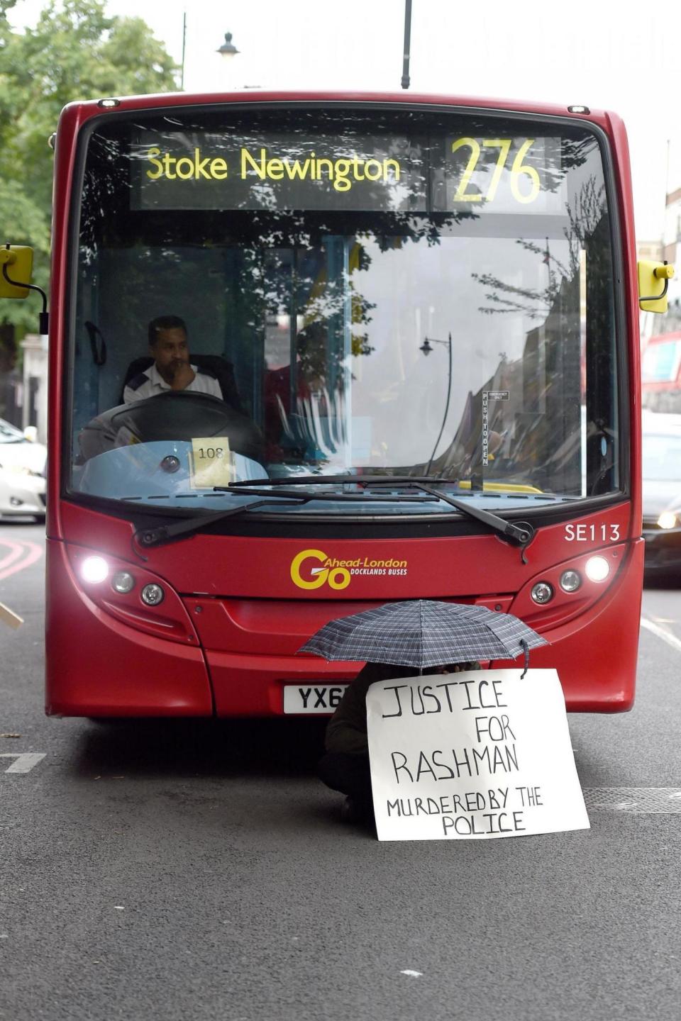 A man sitting in front of a bus under an umbrella to block traffic. (PA)