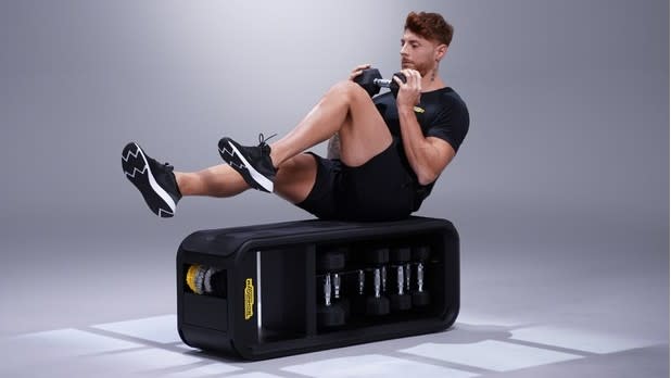 Man performing dumbbell alternating leg raises on Technogym bench against grey backdrop