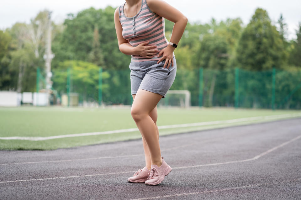 Person in athletic wear taking a break on a track field, hand on hip, other on abdomen