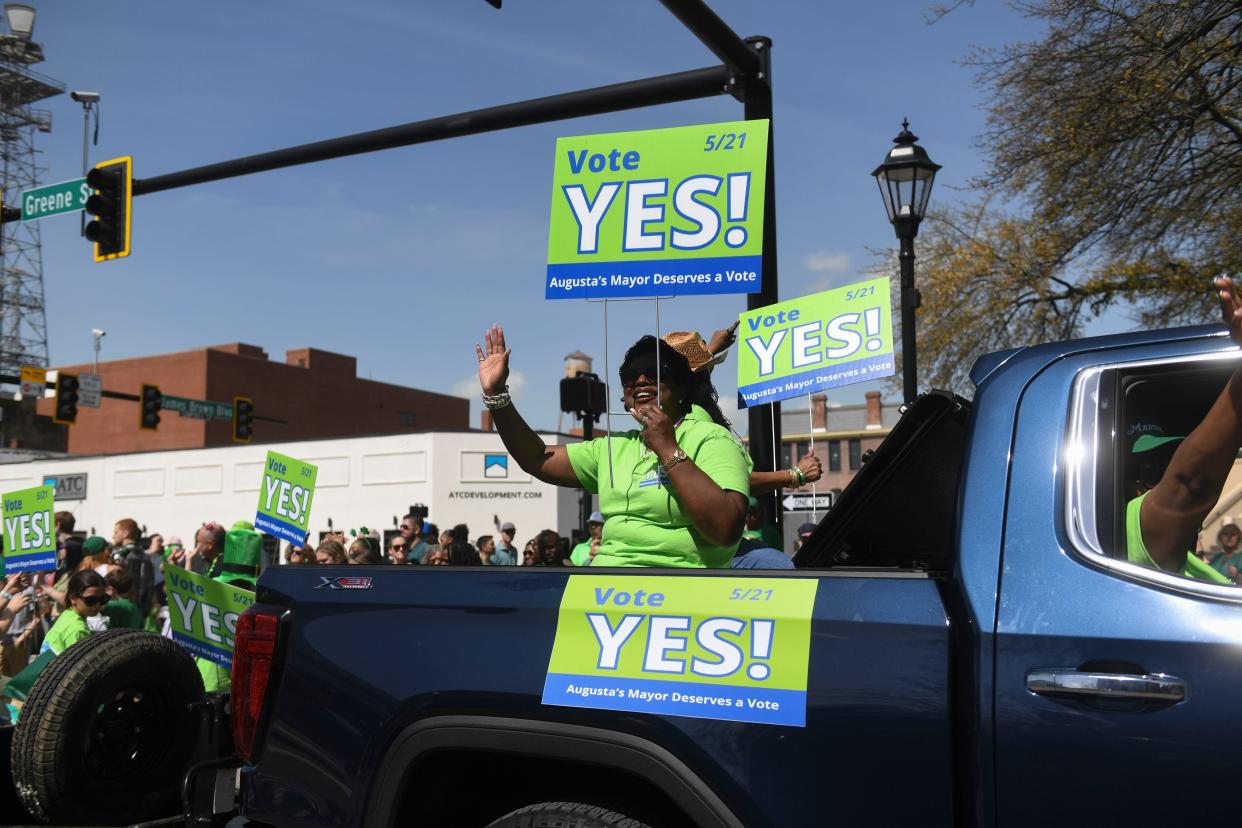 Toni Seals-Johnson, wife of Mayor Garnett Johnson, waves to the crowd in the 46th annual St. Patrick's Day parade through downtown Augusta on Saturday, March 16, 2024.  The signs urged voters to vote "yes" to grant Augusta's mayor a full commission vote.