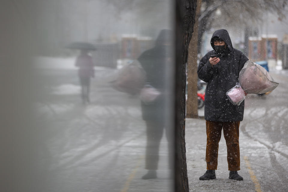 A man wearing a face mask holds a flower bouquet as he stands along a street in Beijing, Friday, Feb. 14, 2020. China on Friday reported another sharp rise in the number of people infected with a new virus, as the death toll neared 1,400. (AP Photo/Mark Schiefelbein)