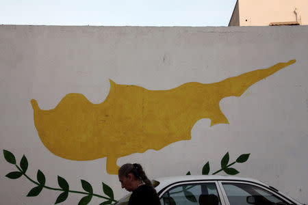 A woman walks in front of Cypriot flag painted on a wall in capital Nicosia, Cyprus November 11, 2016. REUTERS/Yiannis Kourtoglou