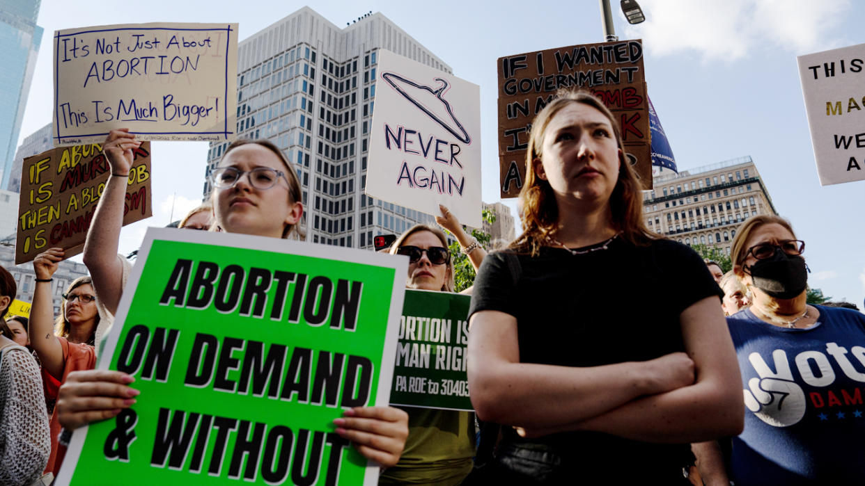 Demonstrators looking glum hold signs saying: Abortion on Demand & WIthout..., Never Again (under a coathanger), It's Not Just About Abortion, This Is Much Bigger.