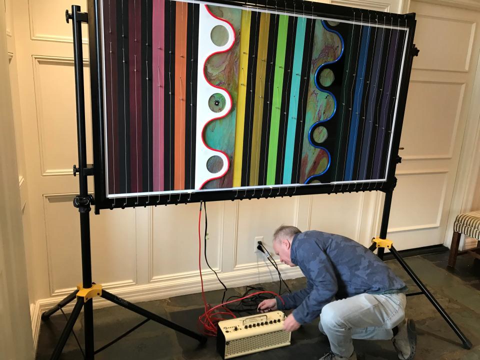 David Bloom, a Ford analyst who creates art on weekends, plugs in an amplifier wired to the 48 electric guitar strings affixed to his artwork, which measures 42 by 69 inches and weighs 350 pounds, at The Community House in Birmingham on Monday, March 18, 2024.