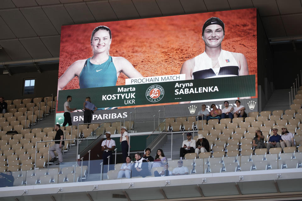 Spectators take their seats under a screen announcing the the first round match of the French Open tennis tournament between Ukraine's Marta Kostyuk and Aryna Sabalenka of Belarus at the Roland Garros stadium in Paris, Sunday, May 28, 2023. (AP Photo/Christophe Ena)